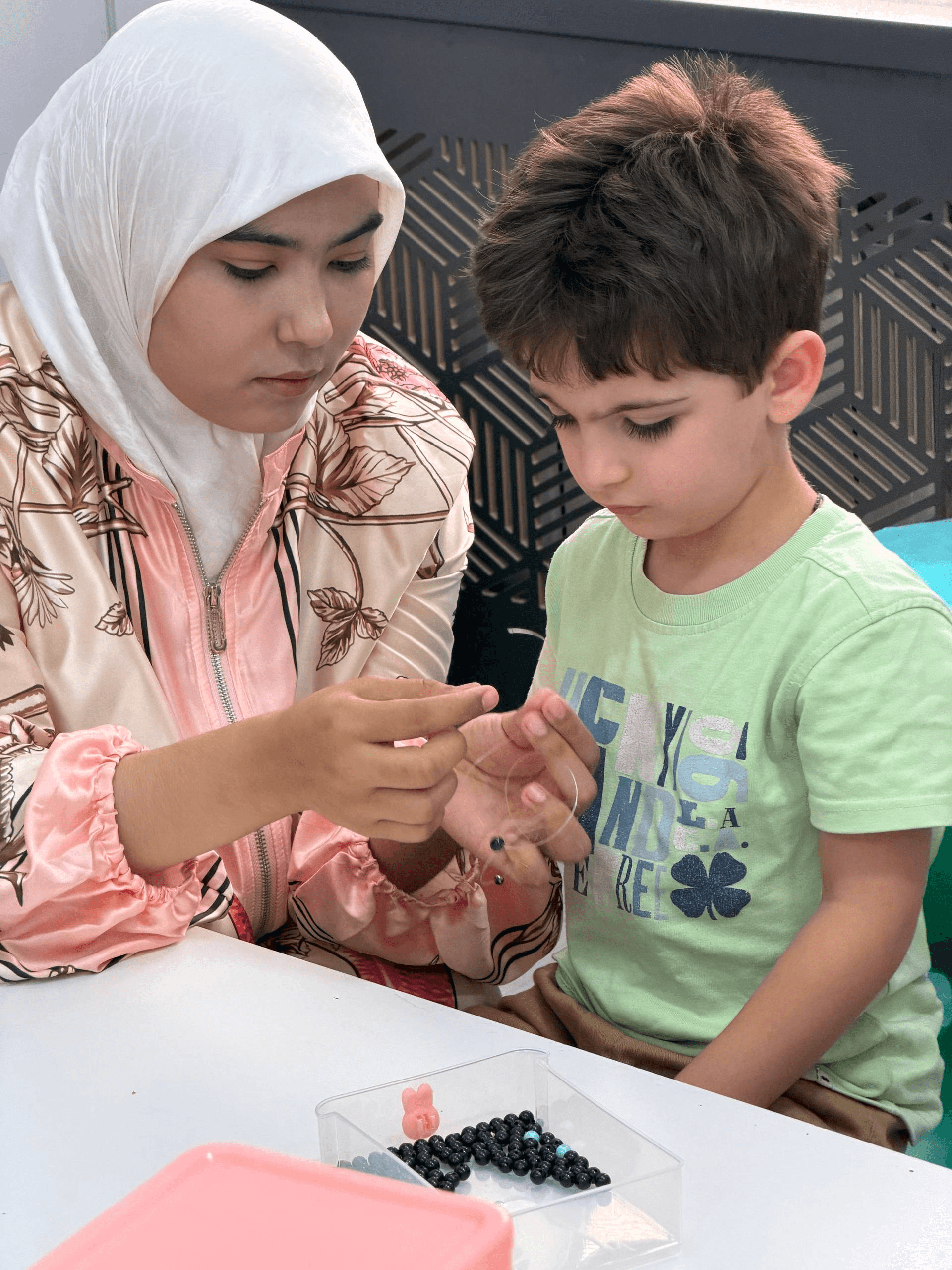 A teacher helping a child with a beading activity at Little Britain Daycare