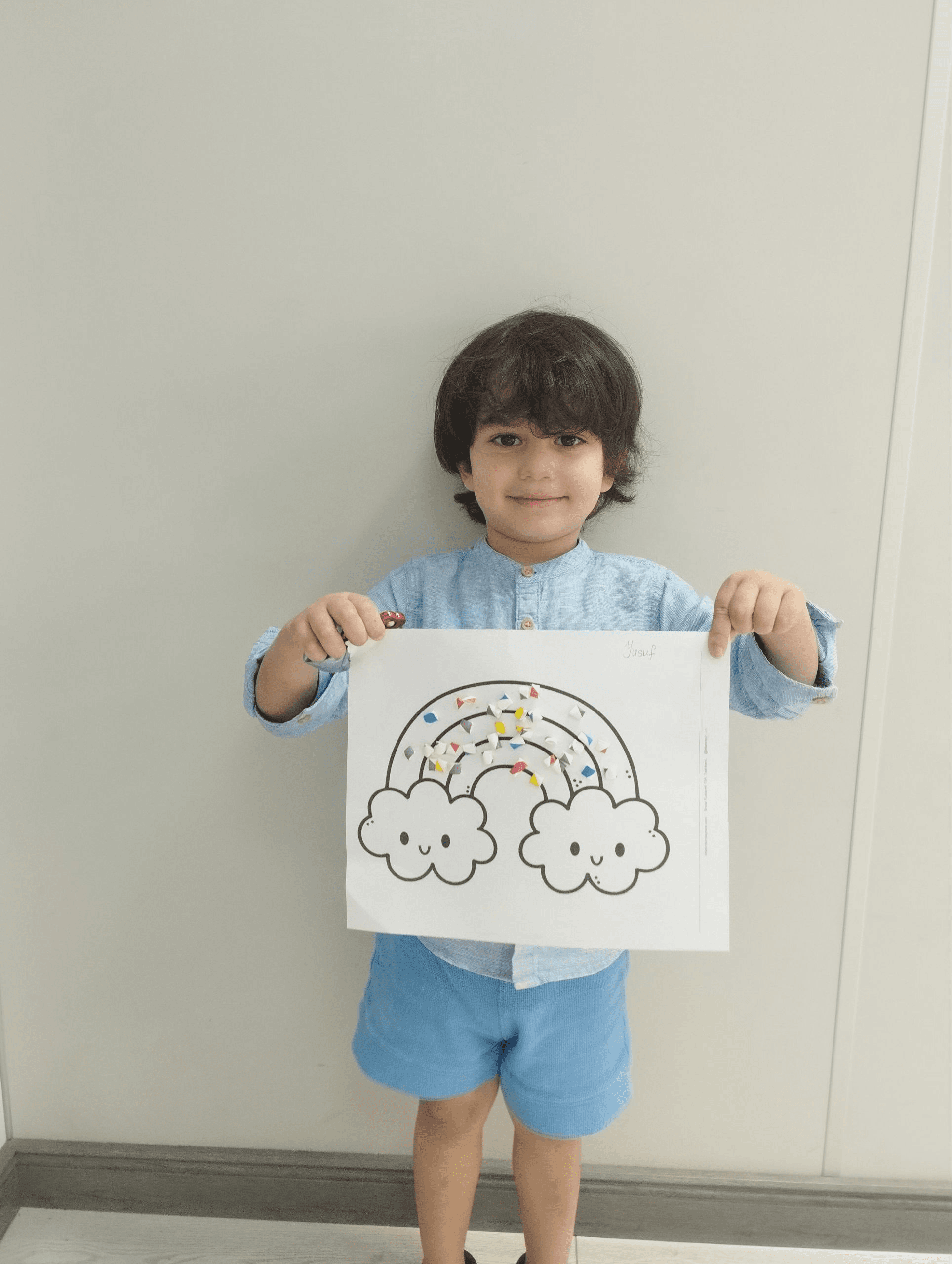 A boy proudly holding up his rainbow craft at Little Britain Daycare