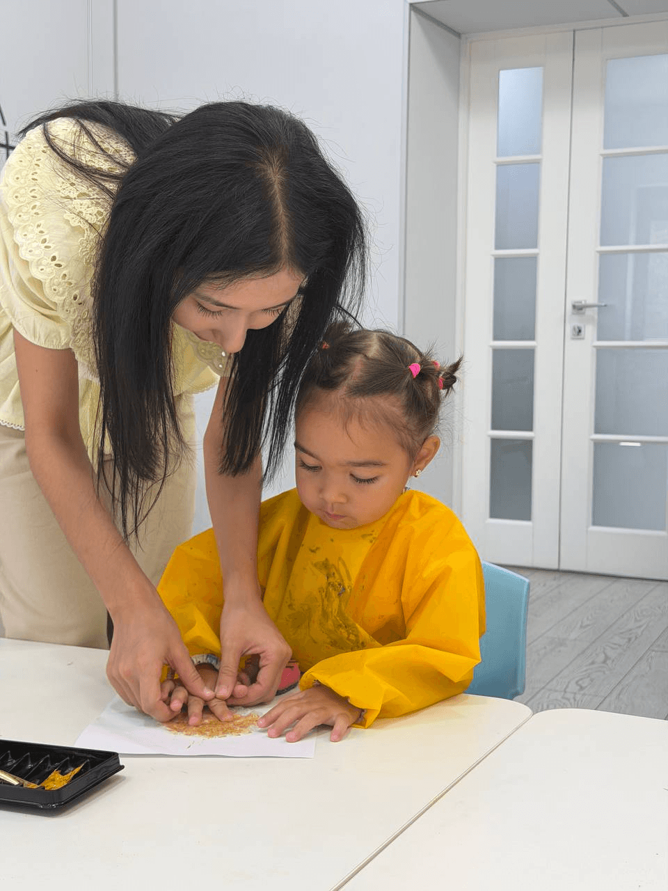 A teacher helping a girl with a craft activity at Little Britain Daycare